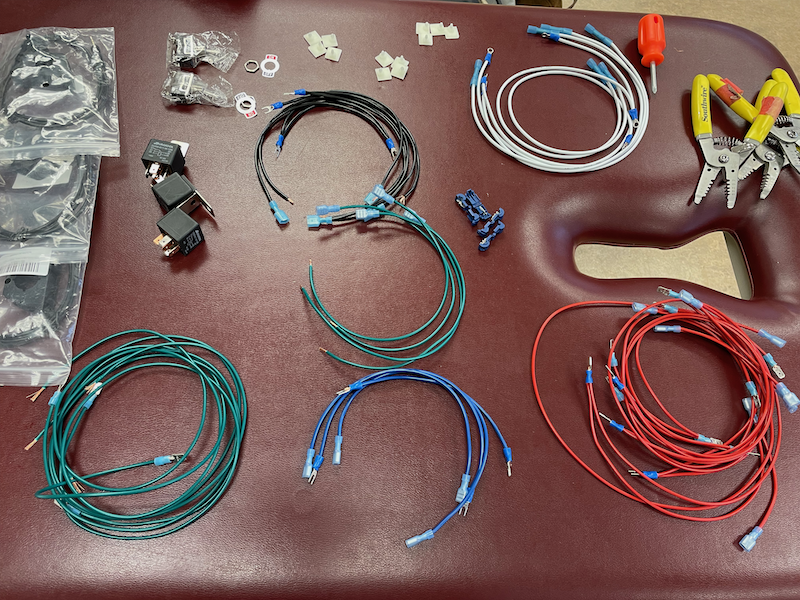 A grouping of supplies, including wires, relay switches, and tools, laid out on a table in preparation for a workshop