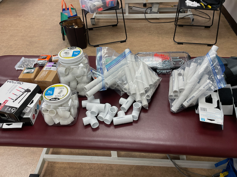 A grouping of supplies, including PVC pipe and velcro, are lined up on a table for a workshop