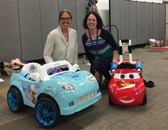 Shawn and Heather, co-directors of UW Go Baby Go, kneeling down between two cars